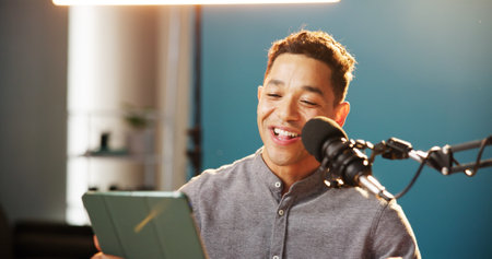 Radio presenter, man and happy with tablet on microphone for live streaming, talk show and online discussion. Male person, content creator and smile as podcast host in studio social media engagementの写真素材