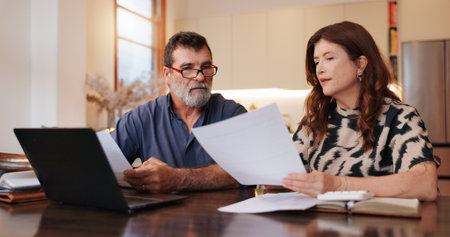 Home, laptop and old couple with paperwork, budget and finance planning in living room. Apartment, senior man and woman with pc, documents or retirement fund with mortgage, savings or property assetsの写真素材