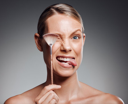 Tongue out, brush or beauty of mature woman in studio for glow, results or transformation on gray background. Facial, joke and playful model with skincare cosmetics for confidence or makeup toolsの写真素材