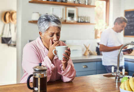 Yawn, morning and coffee with mature woman in kitchen for wake up, caffeine fix and energy. Fatigue, breakfast and tired with senior people drinking at home for retirement, peace and calm togetherの写真素材