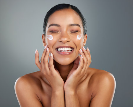 Woman, face and creme with beauty in studio for collagen treatment, skin hydration and skincare. Mockup, happy and cream cosmetics product with hyaluronic acid, retinol or wellness on gray backgroundの写真素材