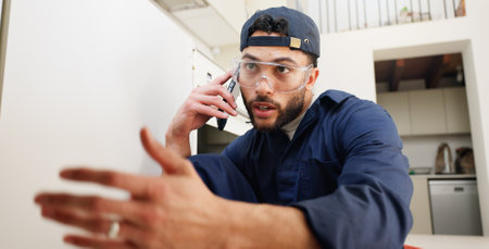 Plumber, worker and man with phone call in kitchen for pipeline problem, leakage repair and sink maintenance. Plumbing contractor, handyman and contact owner for filter system installation in homeの写真素材