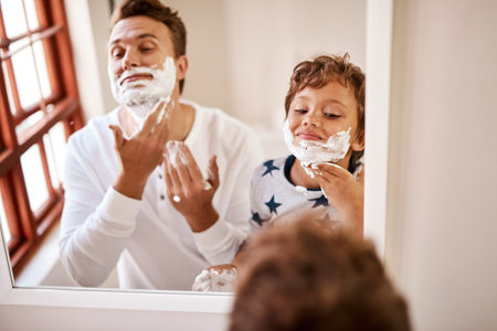 Mirror, boy and cream on face, dad and bonding with child, shaving and teaching in house and grooming. Fun, father and lesson for son, hygiene and kid with man, bathroom and knowledge for skincareの写真素材