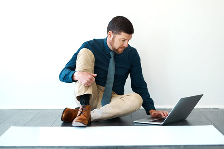 Business, man or architect with laptop on floor for research on building design with wall background mockup space. Professional, person or reading client info for architecture development or planningの写真素材