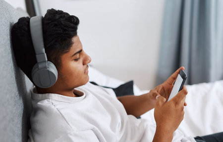 Relax, bedroom and man with smartphone and headphones listening to podcast streaming service. Bed,...