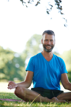 Portrait, yoga and man in park, lotus and smile with wellness, morning routine and zen. Face, person and guy with exercise, outdoor or healthy with break, meditation and chakra with fitness or natureの写真素材