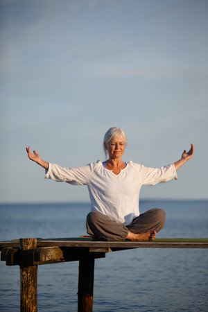 Woman, relaxing and meditation for yoga by ocean with holistic care, spiritual wellness and mindfulness. Mature person, morning and pilates peace, mindset healing and performance with fitness outdoorの写真素材