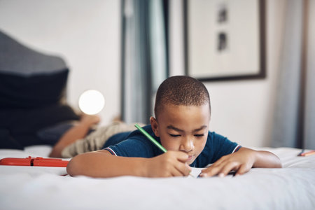 Young boy, writing and lying in bed with book for drawing, sketching or creative activity at home....