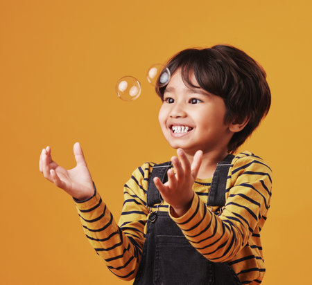Studio, child and playing with bubbles, fun and sensory experience for boy, relax and happy with game. Smile, youth and kid with motor skills, liquid and popping of soap, joy and visual appealの写真素材