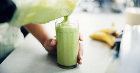 Hands, person and pour liquid in glass in kitchen with organic ingredients, vegan smoothie and...