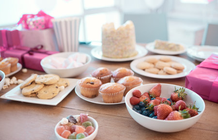 Sweet, treats and table for party at house with birthday celebration, luxury dessert and healthy fruit. Food, cupcake and surprise breakfast with present, sugar cookies and nutrition snack in loungeの写真素材