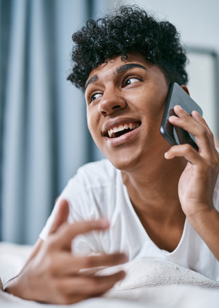 Face, phone call and smile with teen on bed in home for communication, gossip or planning. Conversation, happy and thinking with boy in bedroom of apartment for chat, talking or relax from belowの写真素材