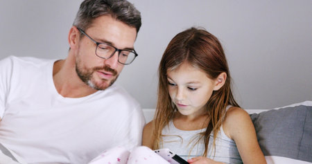 Tablet, father and child in bedroom for learning, education or storytelling in family home together. Dad, girl and kid on digital technology for help with online app, reading ebook or streaming movieの写真素材