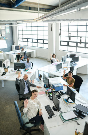 Portrait, above and business people in office, greeting and teamwork with news room. Waving, group and employee with pc, journalist and friendly service with welcome, research for project or magazineの写真素材