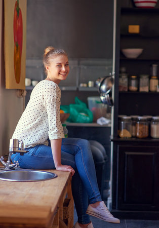 Portrait, smile and woman in kitchen, relax and chilling in weekend, happy and peace in morning and house. Break, cheerful and person in apartment, comfortable and rest on counter, joy and Germanyの写真素材