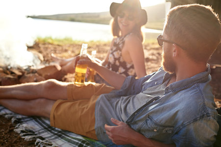 Relax, nature and couple with beer on camp for vacation, getaway or holiday with travel together. Sunglasses, picnic and people with alcohol drink for romantic outdoor date by sunset on weekend trip.の写真素材