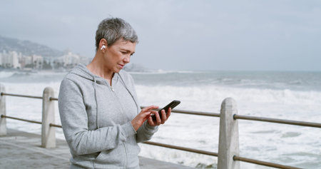 Mature woman, phone and texting on promenade with earphones, reading and workout in morning. Person,...