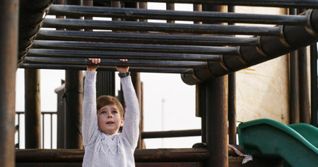 Boy, child and swing on monkey bars at playground, outdoor or adventure with lifting, learning and balance. Kid, memory and exercise on jungle gym at park for challenge, climbing or sunshine in Spainの写真素材