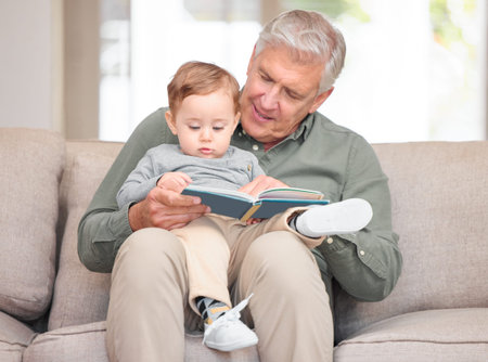 Grandfather, boy and storytelling on sofa in home for fun, bonding and care with education. Grandparent, toddler and kid on learning with book reading for knowledge, information and child growthの写真素材
