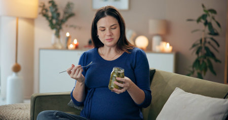 Home, pregnant woman and jar with pickle for eating, nutrition and wellness for baby development. Sofa, female person and hungry with vegetable for pregnancy, craving and healthy snack for vitamin kの写真素材