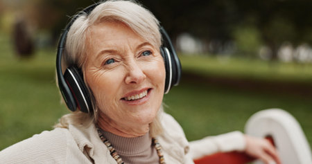 Senior, happy woman or relax with headphones at park for music, audio streaming or radio podcast in...