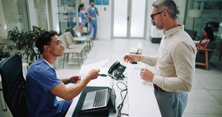 Hospital, nurse and mature man in lobby with paperwork for appointment, consultation and medical service. Healthcare, clinic and patient at admin desk for insurance, application form and documentsの写真素材
