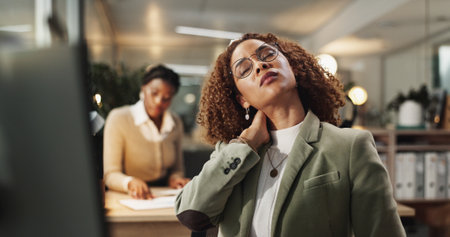 Woman, neck pain and injury at night in office with stress, frustrated or ache at startup company. Person, strain and laptop with muscle fatigue, burnout or tired with bad posture at creative agencyの写真素材
