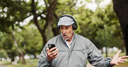 Headphones, senior man and surprised with phone in park for good news, giveaway winner and gambling bonus. Old person, smartphone and shocked for lottery prize, competition notification and shoutingの写真素材
