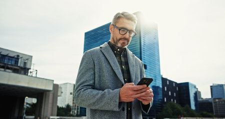 Building, city and phone with mature businessman outdoor for communication, networking or travel....