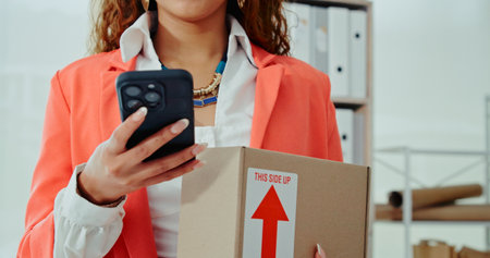 Business woman, hands and box with phone in logistics for online order, delivery or courier service at warehouse. Closeup, female person or distributor on mobile smartphone for package or shipmentの写真素材