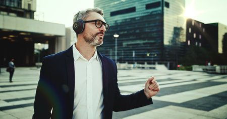 Business, man and music on headphones in city for morning commute, dancing and listening to audio playlist. Mature, professional and walking in urban town with radio, streaming song or travel in roadの写真素材