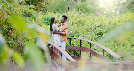 Love, hug and black couple on bridge in park for bonding, connection and outdoor adventure together. Commitment, man and woman on path in nature for romantic date, weekend embrace and green garden.の写真素材