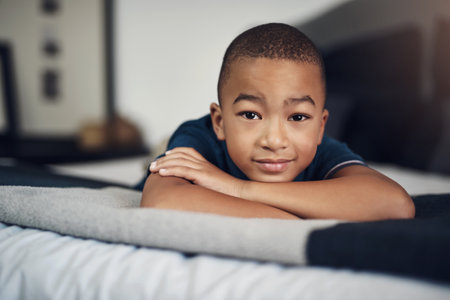 African kid, confident and portrait in bed in home to relax for peace, growth and youth development in apartment. Face, male child and boy in bedroom for calm break and comfort on mattress in Tunisiaの写真素材