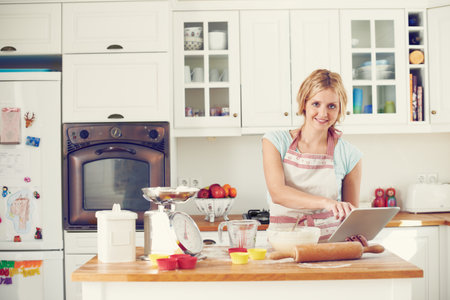 Woman, tablet and portrait in kitchen for baking, cookies and online with video, bowl and streaming. Female person, tech and recipe in home for cooking, cupcakes and food with flour, wheat and tipsの写真素材