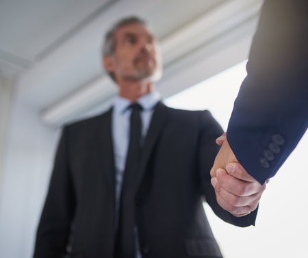 Handshake, partnership and thank you with business people in corporate workplace for deal from below. Agreement, B2B or welcome and employee man shaking hands with colleague in professional officeの写真素材