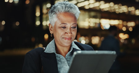 Mature business woman, tablet and city at night, reading or contact on app with smile in street. Person, happy and digital touchscreen for notification, deal and email on urban sidewalk in Costa Ricaの写真素材