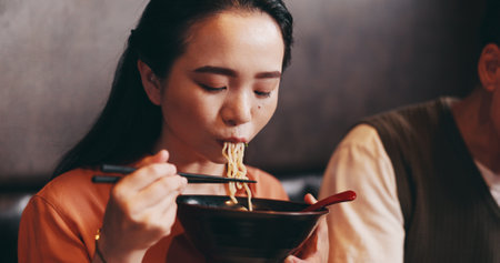 Japanese woman, eating lunch and man in restaurant for date, bonding together and healthy meal. Female person, hospitality and diet with traditional cuisine, chopsticks or ramen noodles as asian foodの写真素材