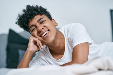 Boy, portrait and happy on bed in home for relax, comfort and weekend with positive mood, peace or cozy. Teenager, face and chilling in bedroom at morning for break, calm and cheerful with leisureの写真素材