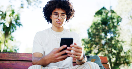 Man, student and smartphone with texting on park bench, reading and break with mobile app in summer. Person, phone and scroll at college with chat, contact and social network at campus in Costa Ricaの写真素材