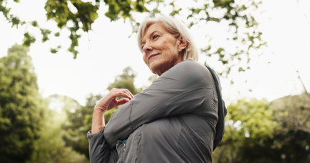 Outdoor, park and mature woman with stretching, smile and calm from exercise and fitness with bottle. Nature, thinking and wellness with idea, training and workout for health in the morning on breakの写真素材