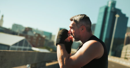Man, boxer and gloves of fitness outdoor with sports exercise, boxing workout and fight performance. Athlete, male person and fist of mma training, defence challenge and match practice on city bridgeの写真素材