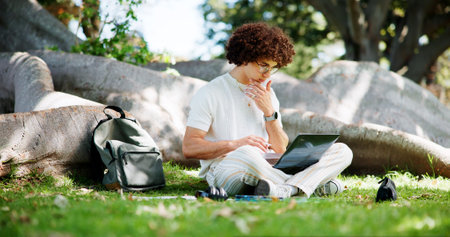 Man, student and laptop for studying at park, lawn and reading with project for online course. Person, computer and e learning on grass for scholarship, exam and education with thinking in Costa Ricaの写真素材