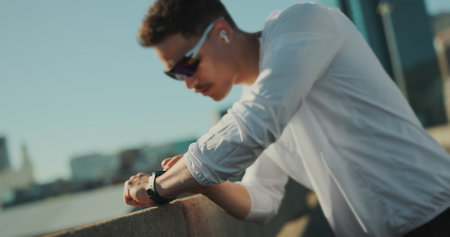 Runner, music and fitness in city on break, thinking and check smart watch for exercise progress. Earphones, bridge and sports man outdoor for health, wellness and listening to podcast for trainingの写真素材