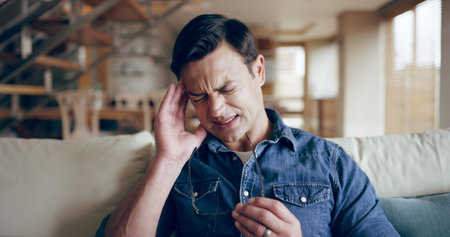Man, stress or headache in home with glasses, sickness and medical condition on sofa. Male person,...