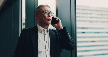 Japanese, businessman and office with phone call for talking, planning or networking with contact. Thinking, male person or mature lawyer with mobile for communication, chat or case detail for clientの写真素材