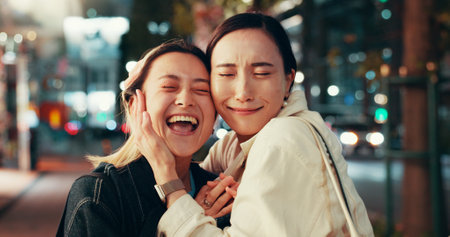 Happy, asian women and night with hug for love, care or bonding together in an urban town or city. Japan, female people or friends with smile in late evening for travel or fun moment in Tokyo streetの写真素材