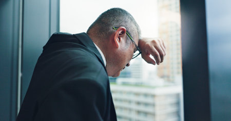 Loss, window or businessman with stress, pressure or debt for bankruptcy, depression or worry. Glass, frustrated director or overwhelmed Japanese boss in office for deadline, job mistake or crisisの写真素材