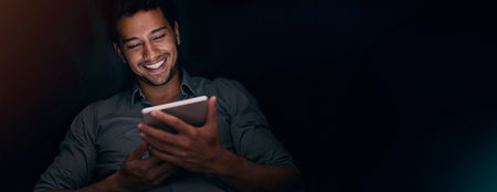 Night, happy and man with tablet, creative and smile for content creation, mockup and browsing. Space, entrepreneur and joy for audience engagement, banner and person with social media in dark officeの写真素材