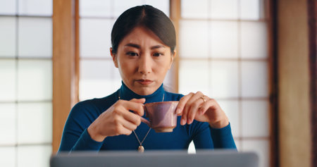 Laptop, tea or Asian woman in home office reading for remote work, research or website. Coffee,...