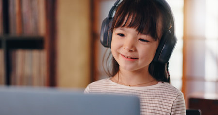 Elearning, video call and child with laptop, headphones and education for girl, listening and smile. Home, happy and online class for kid, studying and scholarship for youth, communication and Japanの写真素材